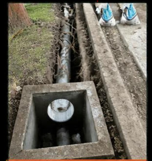 Concrete drainage pit with a pipe connection, next to a new footpath