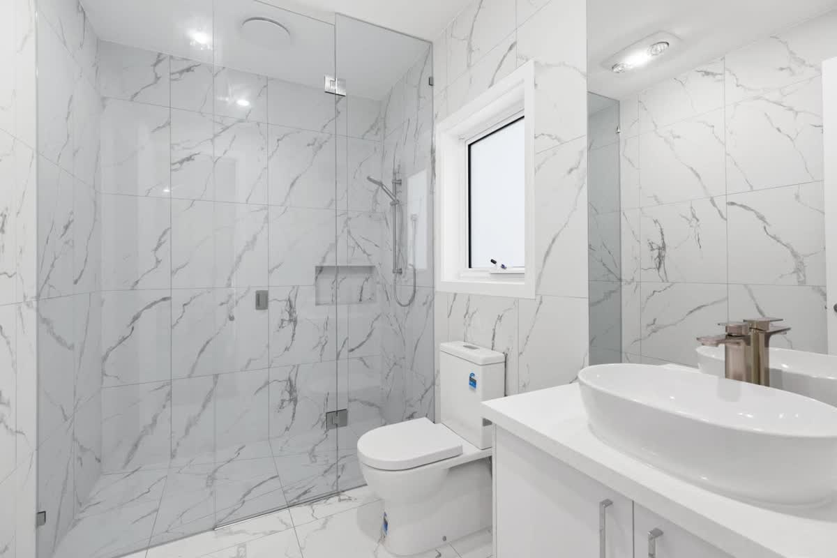 Marble-look tiled bathroom with a frameless shower and a vanity