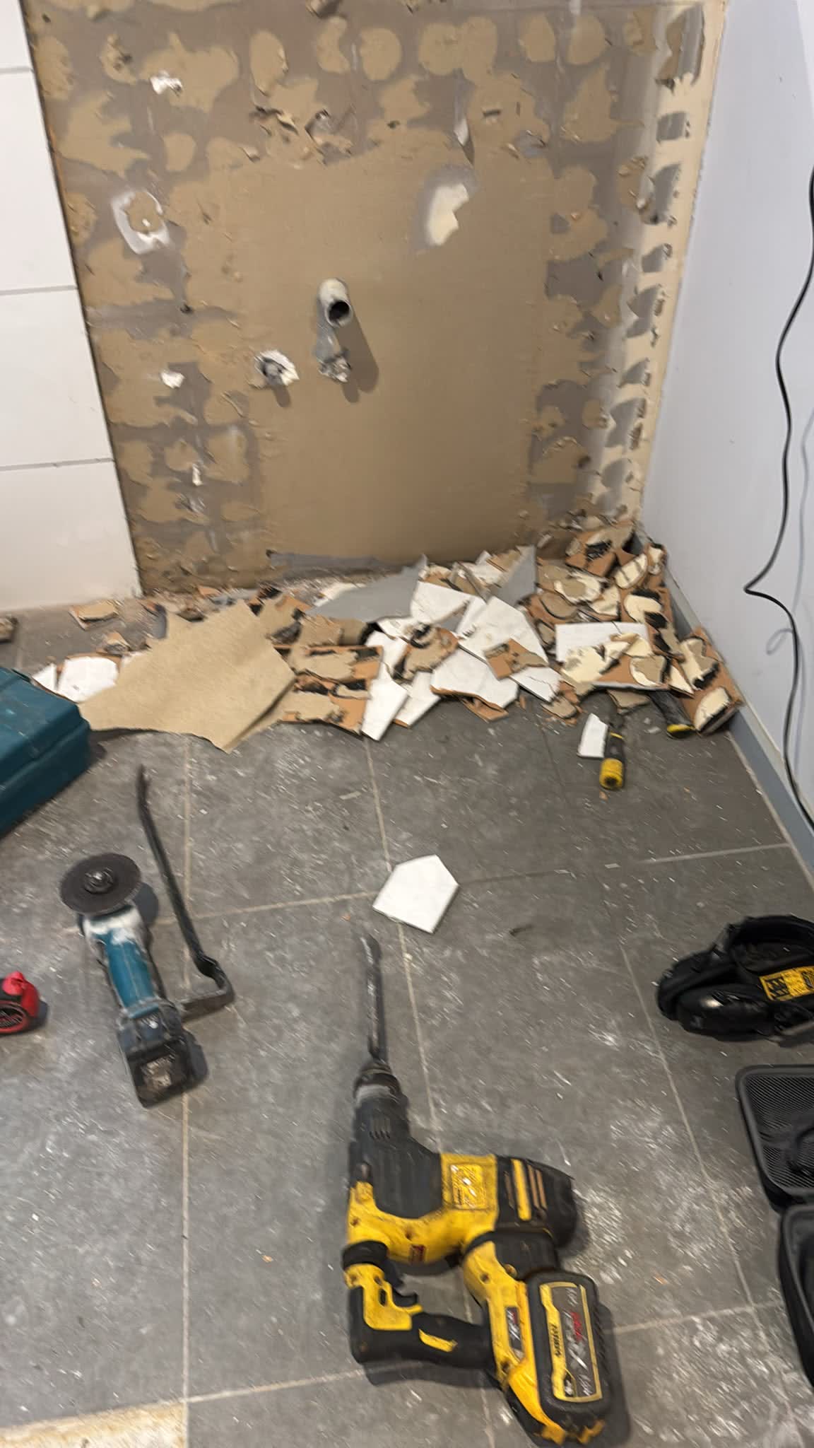 Old tiles stripped from the bathroom walls, with tools on the floor