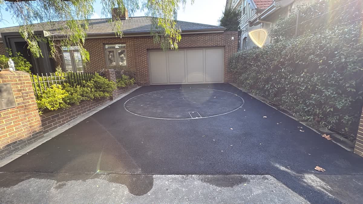 Black asphalt driveway with a circular turntable outline in front of a brick garage